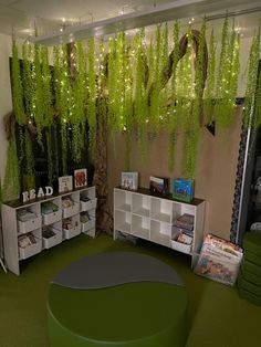 the room is decorated with green plants and bookshelves, while white shelving units are below them