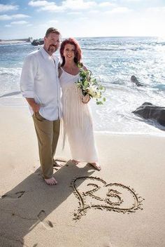 a man and woman are standing on the beach in front of an i love you written in the sand