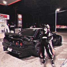 a woman standing next to a black car at a gas station