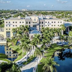 an aerial view of a large building with palm trees in the foreground and water surrounding it