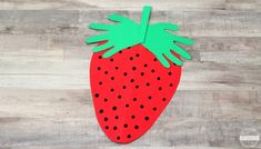 a paper strawberry cut out on top of a wooden table with black dots and green leaves