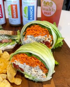 two lettuce wraps filled with meat and vegetables next to chips on a cutting board