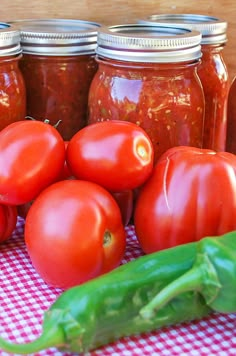 tomatoes and peppers sit on a checkered tablecloth next to jars of tomato sauce