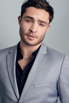 a man in a blue suit and black shirt posing for the camera with his hand on his chest