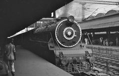 black and white photograph of an old train at a station with people walking on the platform