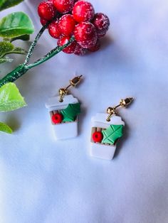 two christmas themed earrings sitting on top of a table next to holly leaves and berries