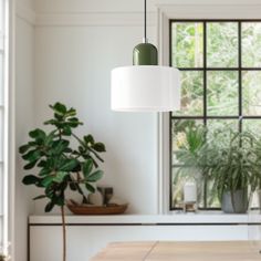 a green lamp hanging over a kitchen table next to a potted plant on a window sill