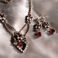 "Necklace: The festoon style was introduced in the early 1900s and this particular theme was given and received by both friends and those with romantic interests. A floral and bow motif, this design is set with garnet and smoke crystal and seed pearls An oval faceted Czech garnet stone dangles inside the heart. An oval prong set stone dangles separately inside the heart. Vintage double twist rope chain connects the pendant and side ornaments. Metal finish is burnished bronze. Necklace Measuremen Double Twist, Heart Vintage, Sweet Romance, Garnet Necklace, Red Jewelry, Garnet Jewelry, Garnet Earrings, Cat Jewelry, Original Jewelry