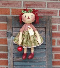 a stuffed doll with red hair wearing a green dress and holding an ornament