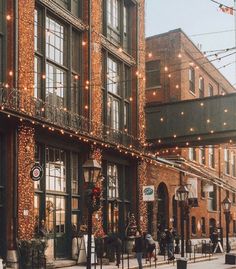 people are walking down the street in front of an old building with christmas lights on it