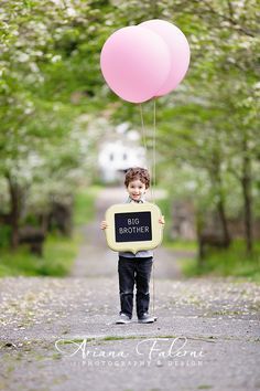 a little boy holding a big brother chalkboard and a pink balloon in the air