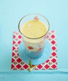 a glass filled with liquid sitting on top of a blue place mat next to a red and white napkin