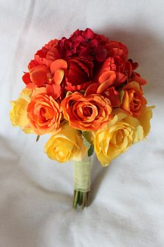 a bridal bouquet with orange and red flowers on a white sheet in the bed