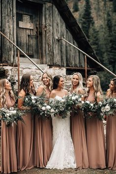 a group of women standing next to each other in front of a wooden building holding bouquets