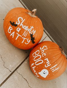 two orange pumpkins with white writing on them sitting on the ground next to each other