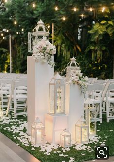 an outdoor ceremony setup with lanterns and flowers on the grass, candles in front of them