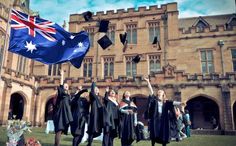 graduates throwing their caps in the air outside an old building with flags and gowns