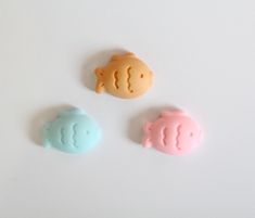 three different colored plastic fish on a white surface, one is pink and one is blue