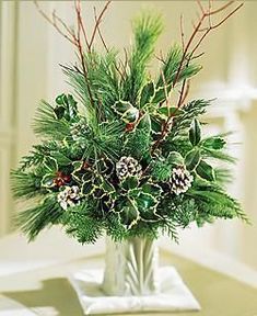 a vase filled with lots of greenery and pine cones on top of a table