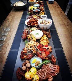 a long table with many different types of food on it, including meats and veggies