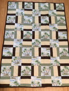 a quilted blanket with palm trees and water in the background on a wooden floor