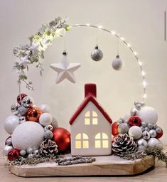 a small white house surrounded by christmas ornaments and lights on a wooden board with a star above it