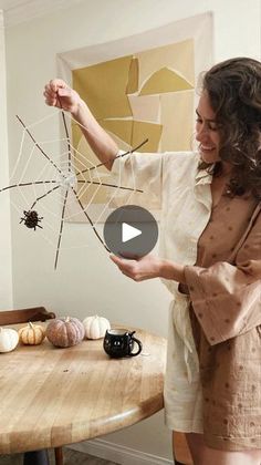 a woman standing in front of a wooden table holding a spider web with her hands