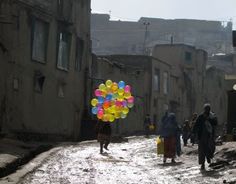 people walking down an alleyway with balloons in the air and buildings on either side