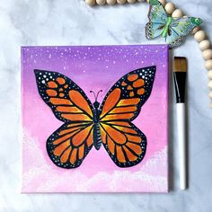 a painting of a butterfly on a pink and purple background next to a wooden bead necklace