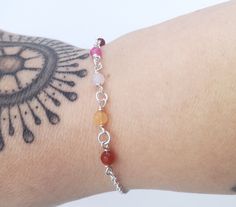 a woman's arm with a tattoo on it and a bracelet that has various colored beads