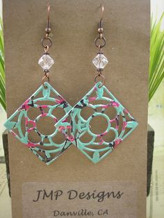 a pair of earrings with pink and blue designs on them sitting on top of a card