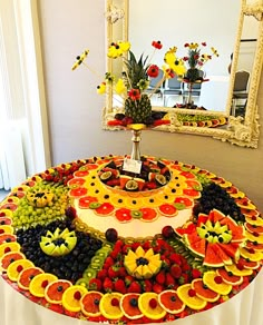 a cake made out of fruit is displayed in front of a mirror with flowers on it