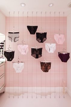 there are many bras hanging up on the wall in this pink and white bathroom