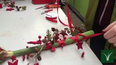 someone is making christmas decorations with red ribbon and pine cones on a white counter top