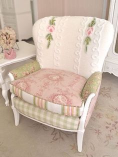 a white chair with pink and green flowers on the armrests next to a mirror