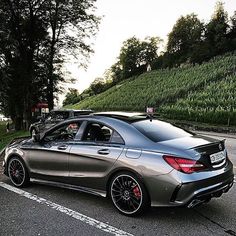 a silver car parked on the side of a road next to a lush green hillside