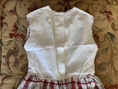 "Vintage cotton dress is made from a white birdseye textured bodice and a red, black, and white gauzy textured skirt gathered into the waist. This same plaid acts as finding along arm holes, neckline and down center front placket, which has 3 decorative black buttons, which look like they may have originally had rhinestones in their centers. It closes with buttons down the center back of bodice- one button is missing. Waistline has a belt carrier on each side. This dress was handmade. Approximat Plaid Sleeveless School Dress, Sleeveless Plaid School Dress, Sleeveless Cotton Plaid Dress, White Sleeveless Cotton Plaid Dress, Sleeveless Fitted Plaid Dress For Daywear, Fitted Sleeveless Plaid Dress For Daywear, White Fitted Plaid Dress For Daywear, Vintage Cotton Dress, White Plaid Skirt