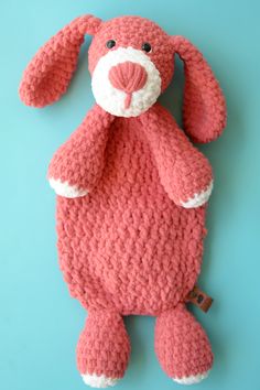 a crocheted pink bunny stuffed animal on a blue background with a tag attached to it's ear