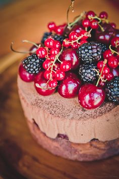 a chocolate cake with berries and blackberries on top is sitting on a wooden table