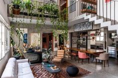 a living room filled with lots of furniture and plants hanging from the ceiling above it