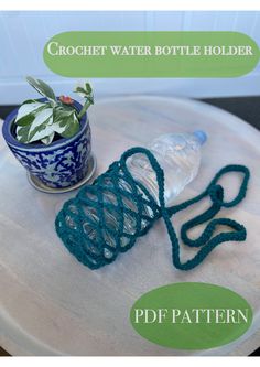 a crochet water bottle holder sitting on top of a table next to a potted plant