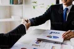 two men shaking hands over papers on a table