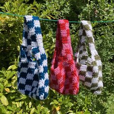 three crocheted mitts hanging on a clothes line in front of some bushes