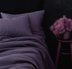 a bed with purple sheets and pillows next to a wooden stool