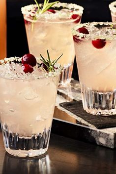 three glasses filled with ice and cherries on top of a wooden table next to a silver tray