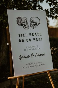 a sign with two skulls on it sitting in front of a tree and fenced area