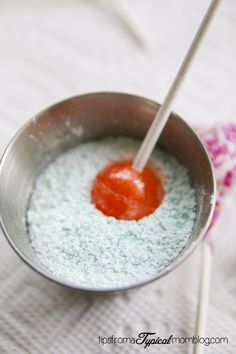 a spoon in a metal bowl filled with powdered sugar and an orange on top