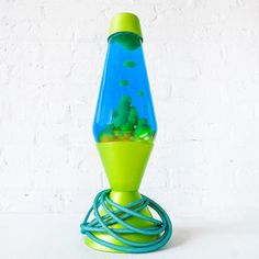 a green and blue vase with rocks in it sitting on a table next to a white wall