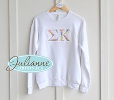 a white sweatshirt with the letter k in sequins on it hanging from a hanger