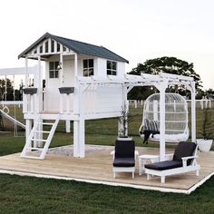 a white swing set in the middle of a grassy area next to a tree house